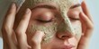 A youthful female applying a exfoliating mask onto her face.