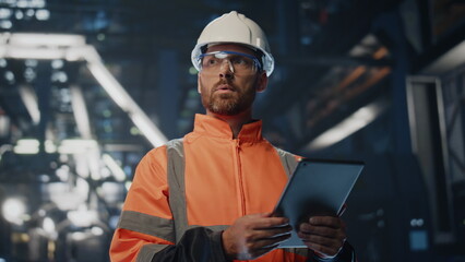 Serious factory supervisor looking at manufacturing making notes tablet close up