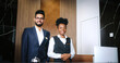 © ihorvsn - Portrait of elegant hotel staff in uniform. Male and female courteous professionals. Indian and African-American hotel receptionists smiling while looking at camera.