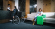 © ihorvsn - Man in wheelchair checking in with help of lovely attractive professional female receptionist ready to assist. Customer care concept. Modern hotel.
