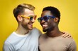 © Shyla Marsare - Pareja de hombres homosexuales con gafas de sol. Novios sobre fondo amarillo. Día del orgullo gay. Colectivo LGTBI.