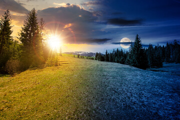 Wall Mural - mountain landscape with sun and moon at spring equinox. meadow on the hillside with coniferous forest. day and night time change concept. mysterious countryside scenery in morning light