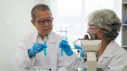 test tube microscope Two senior clinical workers, two men and women in the laboratory, two scientists doing research, young woman and her senior supervisor investigating with microscope and laptop.