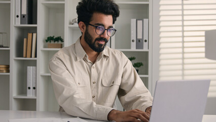 Arabian man Indian muslim ethnic businessman employee stand in corporate office with laptop smiling business entrepreneur millennial male working online with digital data browsing computer internet