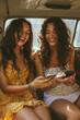 © boyhey - Two women in the backseat of car talking and laughing while holding their phones