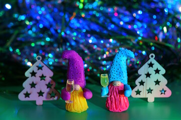 Wall Mural - Two toy dwarfs made of plasticine with glasses of champagne on the background of Christmas decorations. New Year's holidays and Christmas. Decorations and decorations. Green background.