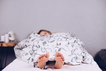 Bare feet of a teenage girl. The girl is lying on the bed covered with a blanket. Foot and heel