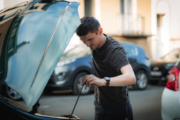 Wall Mural - A young man checks the oil in a car engine with a dipstick.