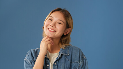 Close-up of young smiling woman dressed in denim shirt isolated on blue background in studio