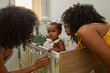 © Edward Córdoba / Andréas Sichel/Stocksy - Baby with mum and granny by crib. The baby looks at the camara
