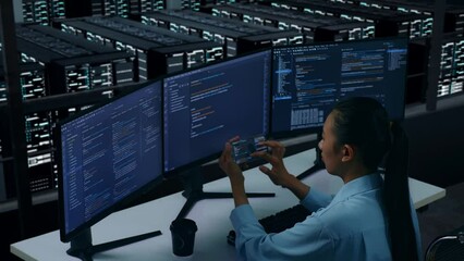 Side View Of Asian Woman Developer Working With Mobile Phone While Write Code With Multiple Computer Screens In Data Center