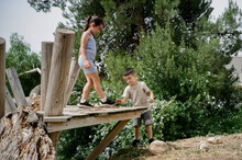 Children Playing On Wooden Bridge In Forest Playground.