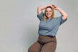 © Danil Nevsky/Stocksy - Happy young plus size woman sitting in room with gray backdrop