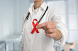 © New Africa - Cancer awareness. Doctor holding red ribbon on blurred background, closeup