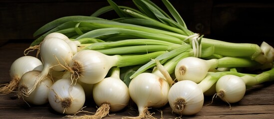 Wall Mural - A collection of onions and green onions are stacked on a wooden table. The onions are round and brown, while the green onions have long green stems and white bulbs.