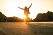 © Luis Herrera/Stocksy - carefree woman walking on the beach at sunset with arms up