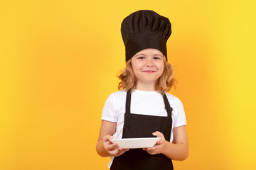 Wall Mural - Funny child cook with cooking plate. Kid chef cook, studio portrait. Children cooking. Kid boy with apron and chef hat.