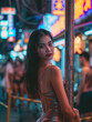 Beautiful sexy asian girl woman tanned skin looking at the camera standing next to a metal pole at night in a busy street nightlife party
