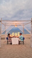 Wall Mural - A man and a woman are enjoying the beach view at a table, smiling and relaxing in the shade. Outdoor furniture adds to their leisurely travel experience romantic, Valentine, dinner, Hua Hin ,Thailand