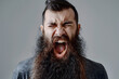 Close up portrait of angry mad young man with long beard shouting isolated on light grey background