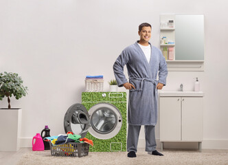 Poster - Young man in a robe posing in a bathroom with a green power efficient washing machine