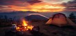 The enchanting warmth of a campfire and tea pot, accompanied by a tent, with the silhouette of mountains against a vibrant sunset sky.