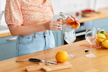 drinks and people concept - close up of woman pouring liquor from glass bottle to jigger and making cocktail at home kitchen