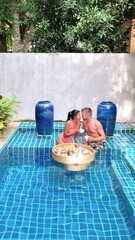 Wall Mural - A man and a woman are sharing leisure time in a rectangular swimming pool surrounded by plants and trees, enjoying the aqua recreation at a real estate property