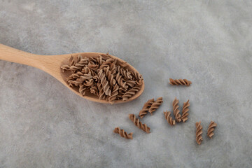 Pasta di Lino or Flaxseed gluten free pasta in spoon on grey background, close-up. Low glycemic index food. Fusilli made from flax and corn flour