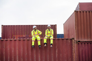 Two men in yellow and white safety gear are sitting on top of a stack of shipping containers. Concept of camaraderie and teamwork