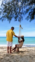 Wall Mural - A man and a woman in shorts are happily swinging together on the beach, with the water, sky, and landscape creating a picturesque scene. Koh Kood Island Thailand