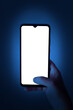 Female hand holdinga smartphone at night. Phone with white screen on defocused dark blue background. There is a work path in the file.