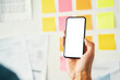 © baranq - Web designer holding phone with white mockup screen with planning board in background