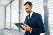 © baranq - Smiling businessman in suit using digital tablet in office