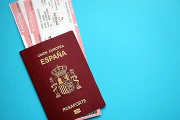 Red Spanish passport of European Union with airline tickets on blue background close up. Tourism and travel concept