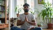 fitness, meditation and healthy lifestyle concept - Indian man in earphones listening to music on smartphone and meditating in lotus pose at home