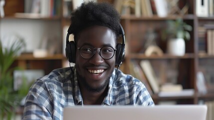 Wall Mural - Happy millennial African American man in glasses wearing headphones, enjoying watching the educational webinar on his laptop. 