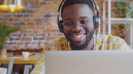 Wall Mural - Happy millennial African American man in glasses wearing headphones, enjoying watching the educational webinar on his laptop. 