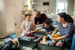 © Marko Geber - Family packing suitcase together for vacation in living room