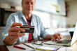 © Marko Geber - Middle aged man holding a credit card using laptop at home