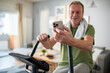 © Marko Geber - Middle aged man using smartphone on home exercise bike