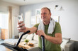 © Marko Geber - Middle aged man using smartphone on home exercise bike