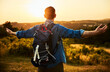© baranq - man enjoying summer sunset during backpacking trip standing with arms outstretched