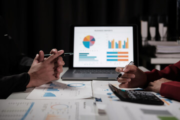 Fototapete - Two people are looking at a laptop screen with a business graph on it