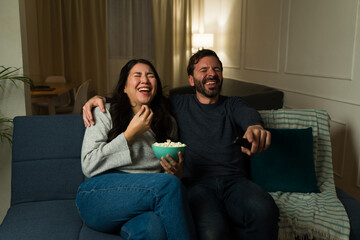 Wall Mural - Cheerful couple watching a movie and laughing relaxing on the couch