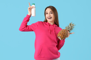 Wall Mural - Young woman with bottle of tasty yoghurt and pineapple on blue background