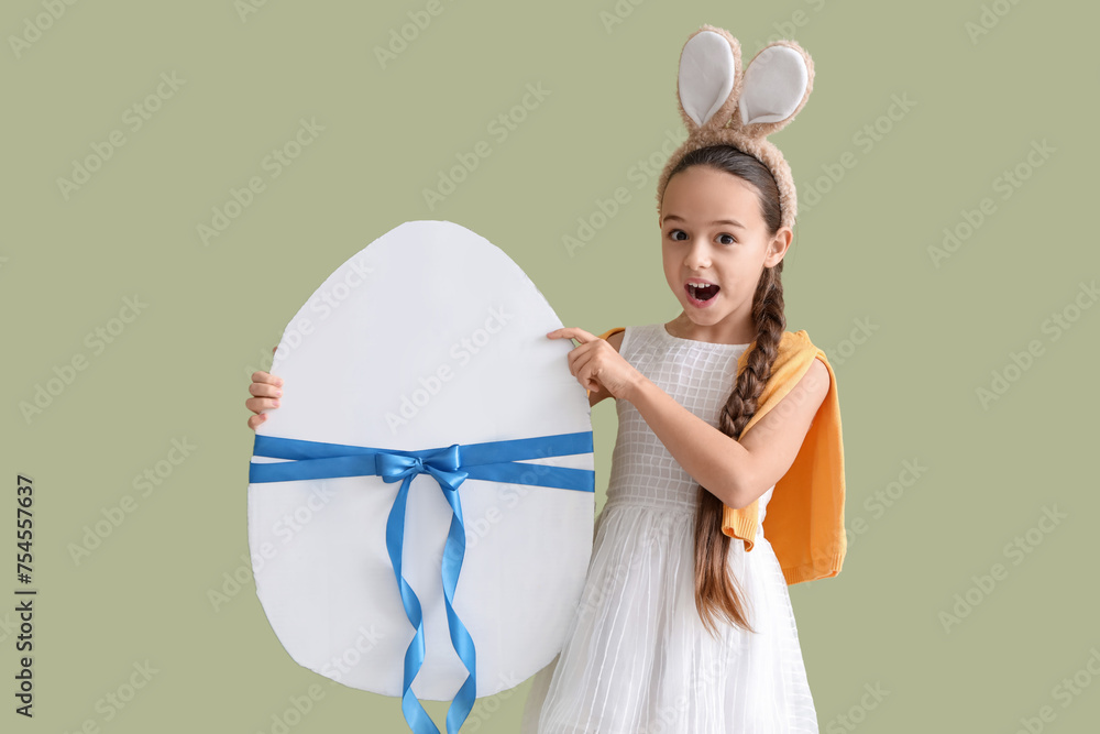 Cute little girl with bunny ears and big Easter egg on green background
