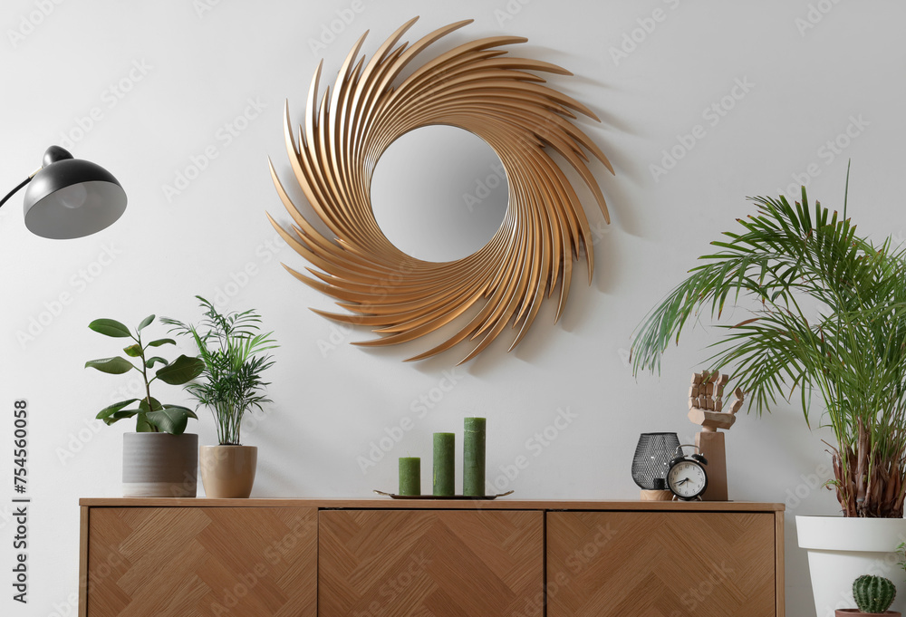 Interior of living room with golden mirror, commode and plants