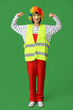 © Pixel-Shot - Young laughing female builder with clown nose on green background. Fool's day