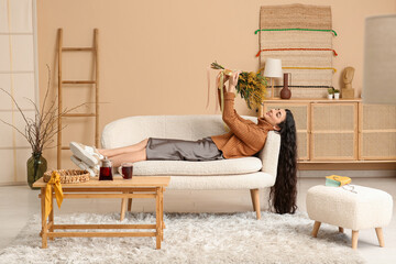 Wall Mural - Beautiful young woman with bouquet of mimosa flowers on sofa in living room